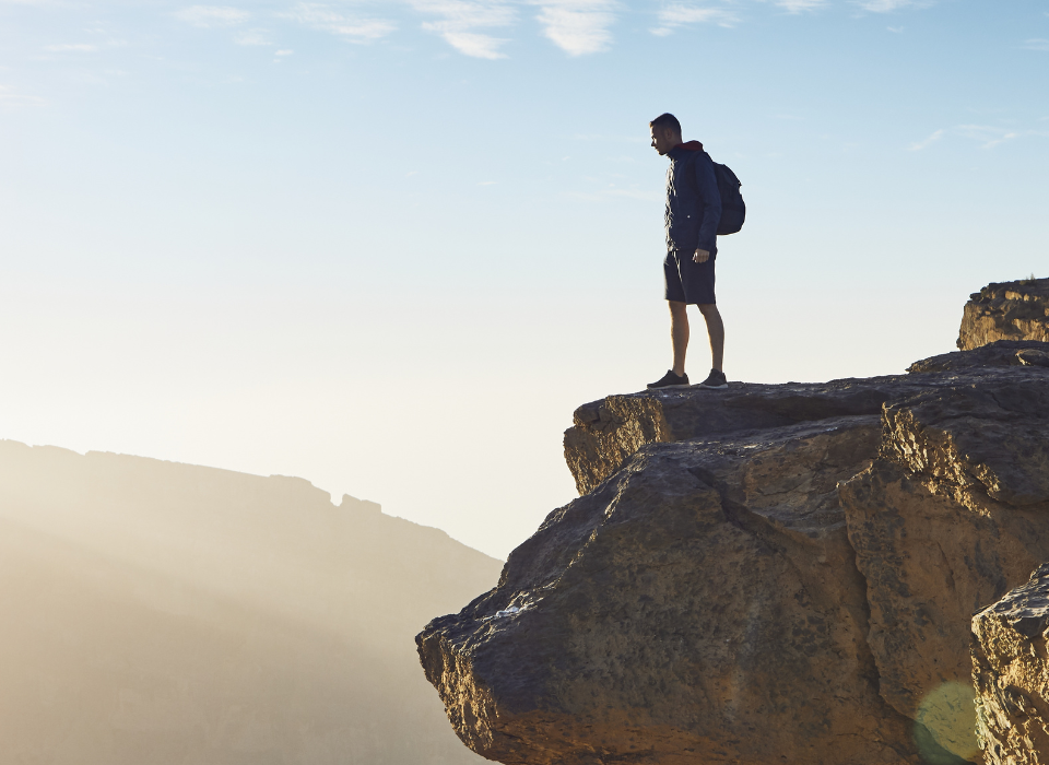 Man standing on a cliff edge with a blue sky backdrop