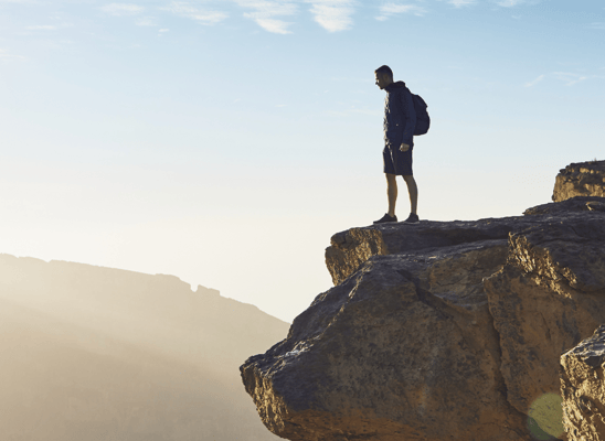 Man standing on a cliff edge with a blue sky backdrop