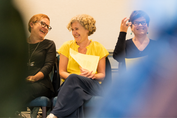 Three women sat together, two are laughing and looking at each other