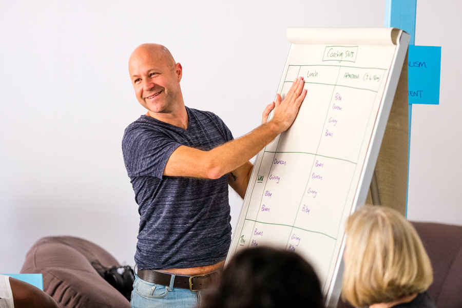 A man stood at a flipchart presenting to an audience. The image shows the top of the back of their heads.