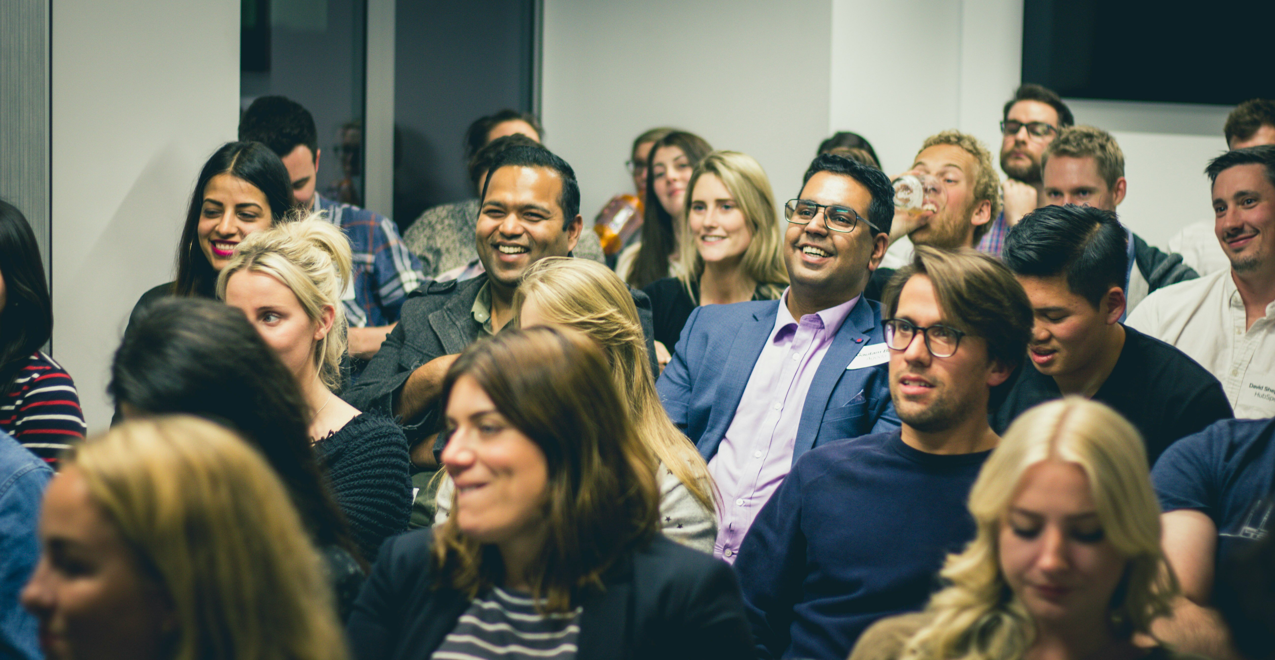 A group of people at work, all sat facing one direction, they are smiling, some are laughing